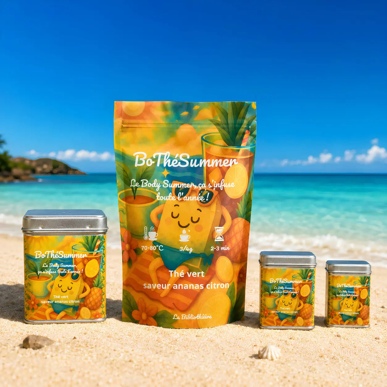 Gamme complète de thé vert ananas citron : boîtes en métal et sachets recharge posés sur le sable face à la mer.
