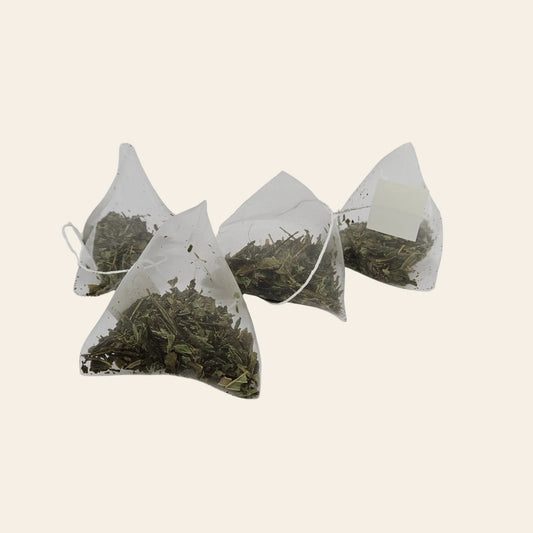 Sachets pyramides de thé vert à la menthe montrant la coupe fine des feuilles de Sencha et les éclats de menthe séchée.